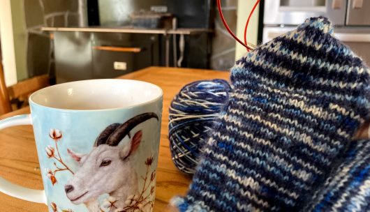 sock knitting on red needles with goat mug