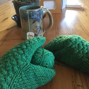 person wearing green mittens with mug of tea