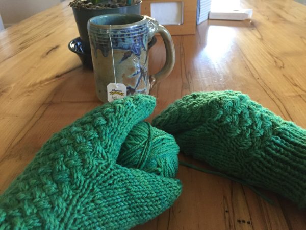 person wearing green mittens with mug of tea